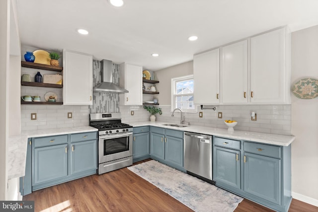 kitchen featuring blue cabinets, sink, appliances with stainless steel finishes, wall chimney range hood, and white cabinets