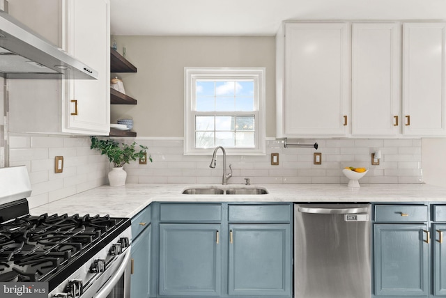 kitchen with appliances with stainless steel finishes, white cabinetry, sink, blue cabinetry, and wall chimney exhaust hood