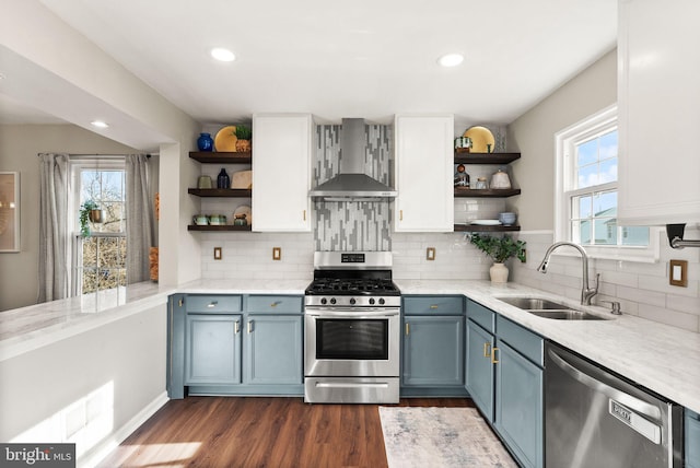 kitchen featuring blue cabinets, sink, white cabinets, stainless steel appliances, and wall chimney range hood