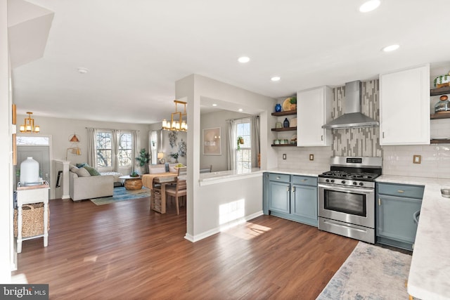 kitchen featuring stainless steel range with gas cooktop, pendant lighting, white cabinetry, wall chimney range hood, and an inviting chandelier