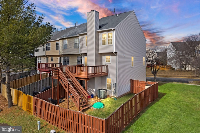 back house at dusk featuring cooling unit, a deck, and a lawn