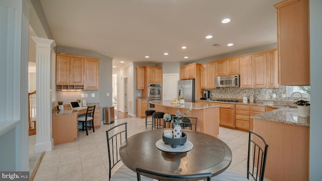 kitchen featuring sink, appliances with stainless steel finishes, backsplash, light stone countertops, and a kitchen island