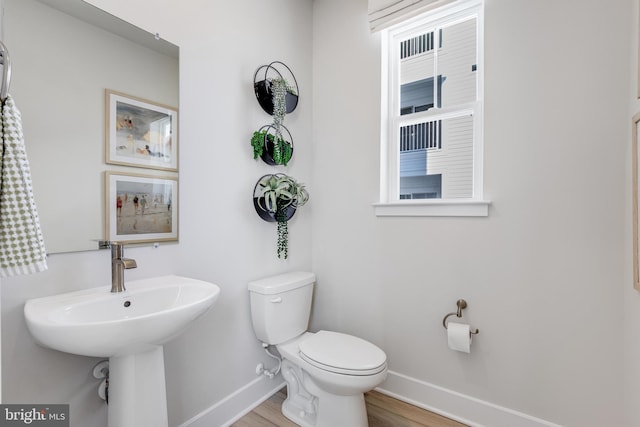 half bath with toilet, baseboards, and wood finished floors