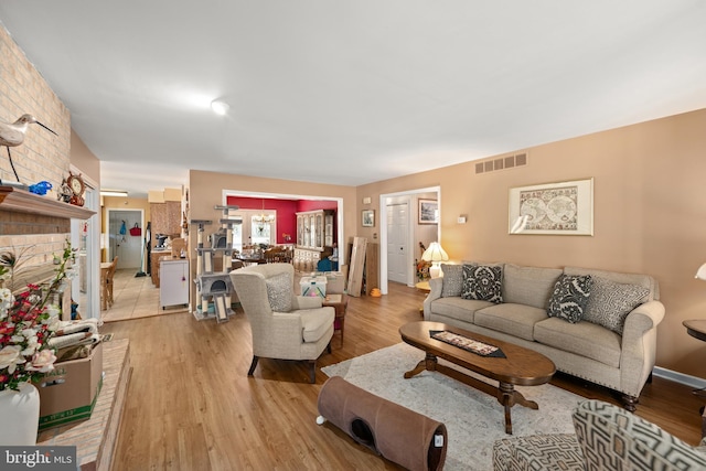 living area with light wood-style floors, a brick fireplace, and visible vents