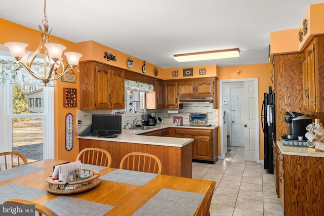 kitchen featuring light tile patterned floors, a peninsula, light countertops, under cabinet range hood, and a sink