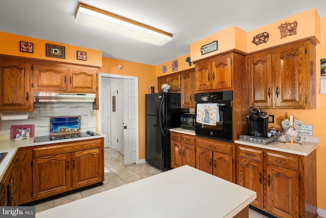 kitchen featuring black appliances, brown cabinetry, light countertops, and under cabinet range hood