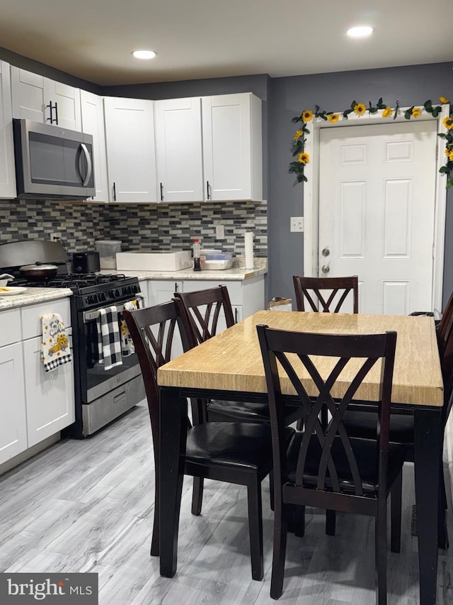 kitchen with white cabinetry, appliances with stainless steel finishes, backsplash, and light wood-type flooring