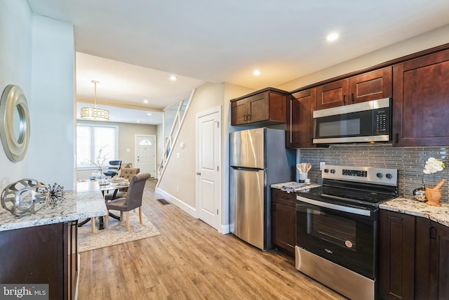 kitchen featuring stainless steel appliances, pendant lighting, light wood-type flooring, and decorative backsplash