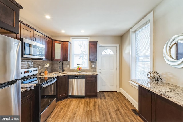 kitchen featuring sink, light stone counters, light hardwood / wood-style flooring, appliances with stainless steel finishes, and backsplash