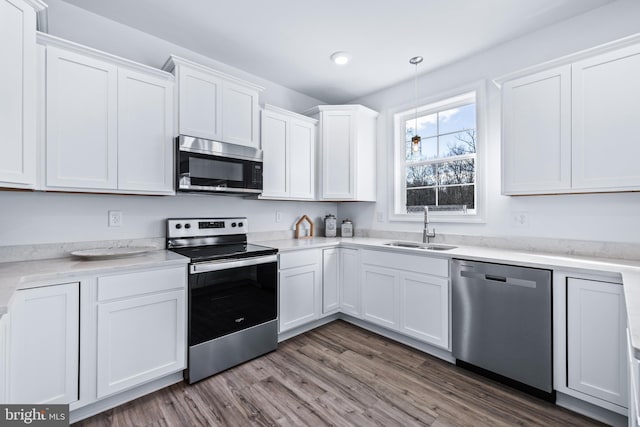 kitchen with sink, dark wood-type flooring, appliances with stainless steel finishes, white cabinetry, and decorative light fixtures