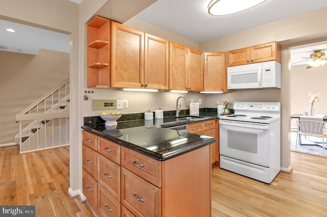 kitchen with sink, dark stone counters, ceiling fan, white appliances, and light hardwood / wood-style flooring