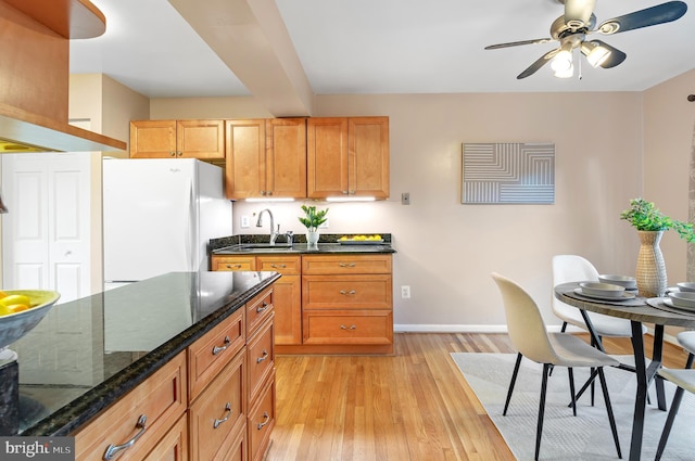 kitchen featuring sink, dark stone counters, white refrigerator, ceiling fan, and light wood-type flooring