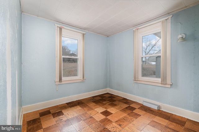 empty room with crown molding, plenty of natural light, and parquet flooring