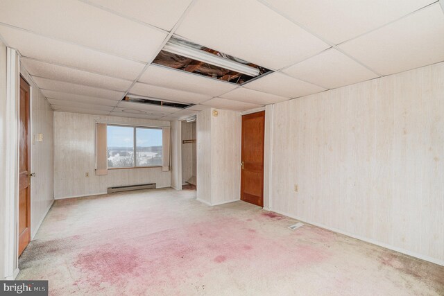 unfurnished room featuring a baseboard heating unit, a paneled ceiling, wooden walls, and carpet