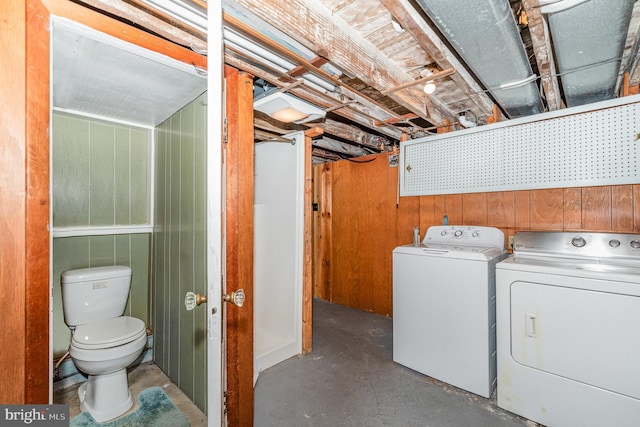 clothes washing area with washing machine and clothes dryer and wood walls