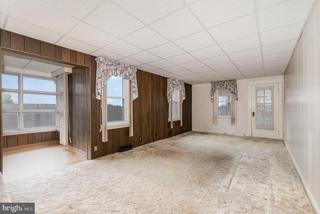 carpeted spare room featuring a drop ceiling and wooden walls