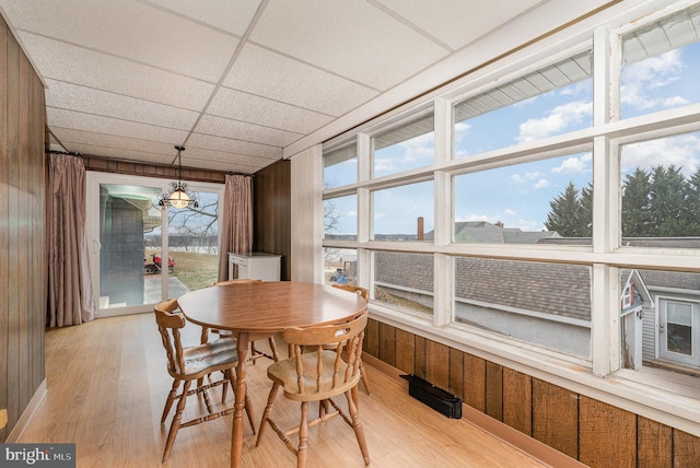 dining area featuring wooden walls, a drop ceiling, and light wood-type flooring