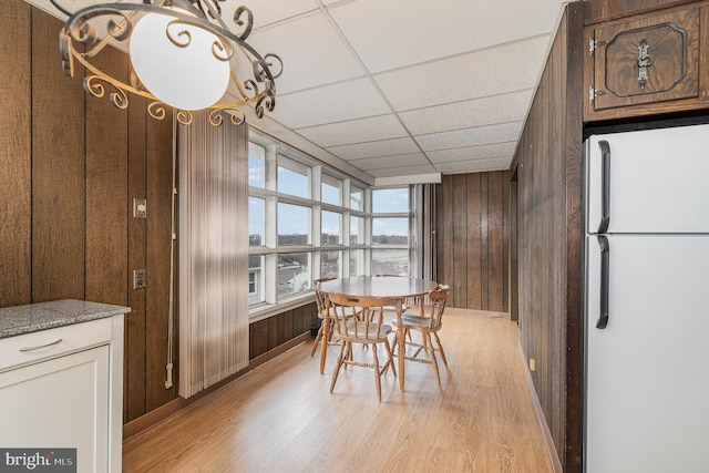 dining room featuring a drop ceiling, light wood-type flooring, and wood walls