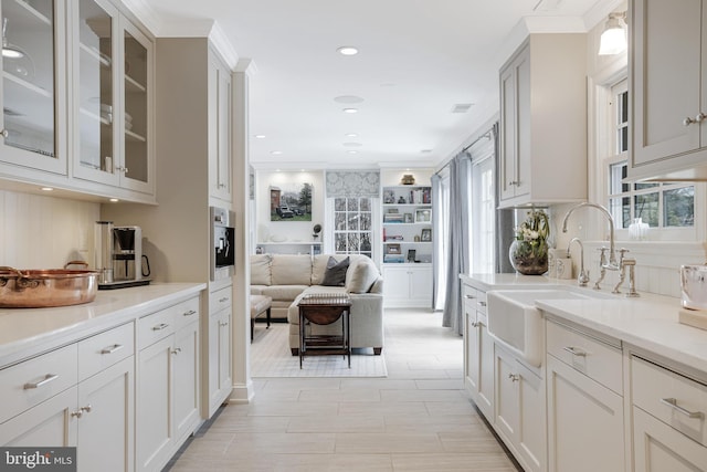 kitchen with a sink, stainless steel oven, open floor plan, glass insert cabinets, and crown molding