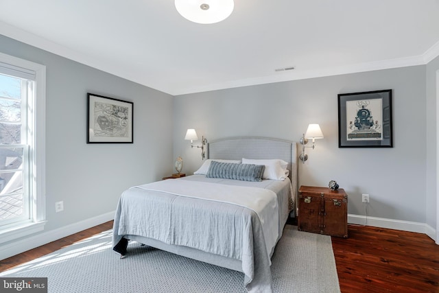 bedroom with multiple windows, visible vents, baseboards, and wood finished floors