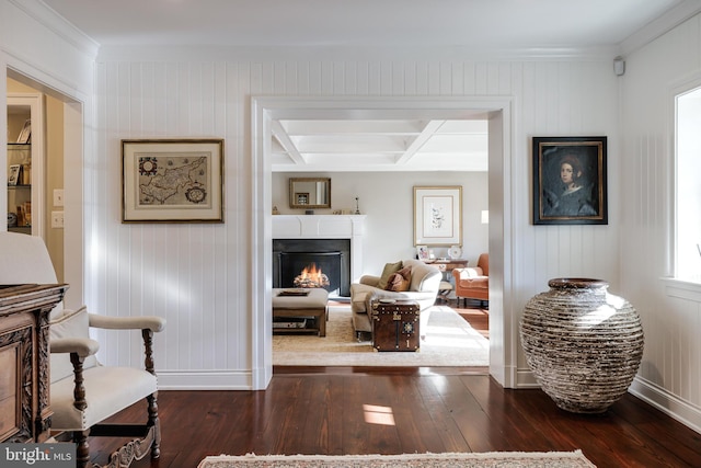 living area featuring dark wood finished floors, coffered ceiling, beamed ceiling, a lit fireplace, and baseboards