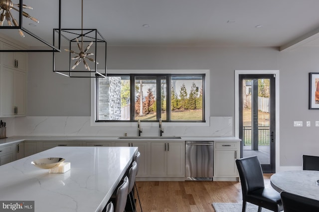 kitchen with decorative light fixtures, sink, stainless steel dishwasher, light stone counters, and light wood-type flooring