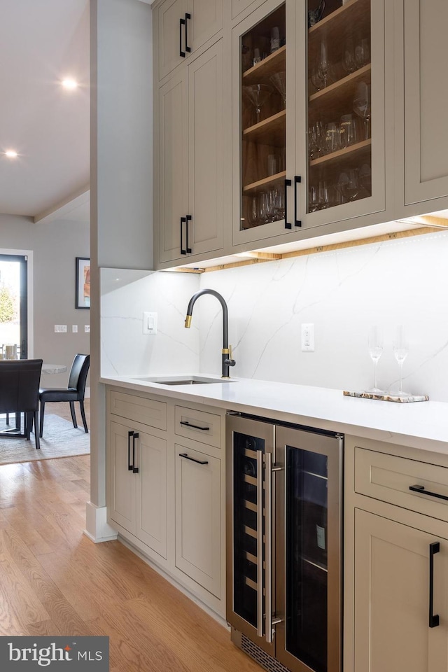 bar with tasteful backsplash, sink, light hardwood / wood-style flooring, and beverage cooler