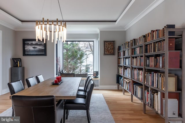 dining space with ornamental molding, a raised ceiling, and light hardwood / wood-style flooring