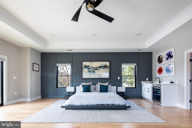 bedroom featuring wet bar, a tray ceiling, light hardwood / wood-style floors, and beverage cooler