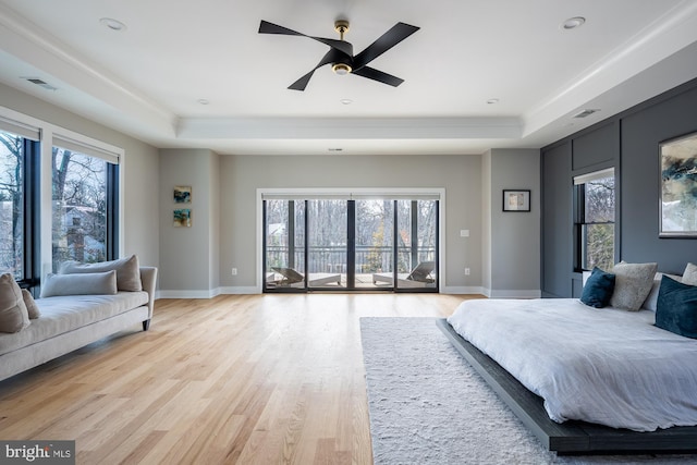 bedroom with ceiling fan, a raised ceiling, light hardwood / wood-style floors, and access to outside