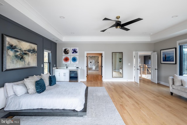 bedroom with wine cooler, a raised ceiling, indoor wet bar, and light hardwood / wood-style flooring