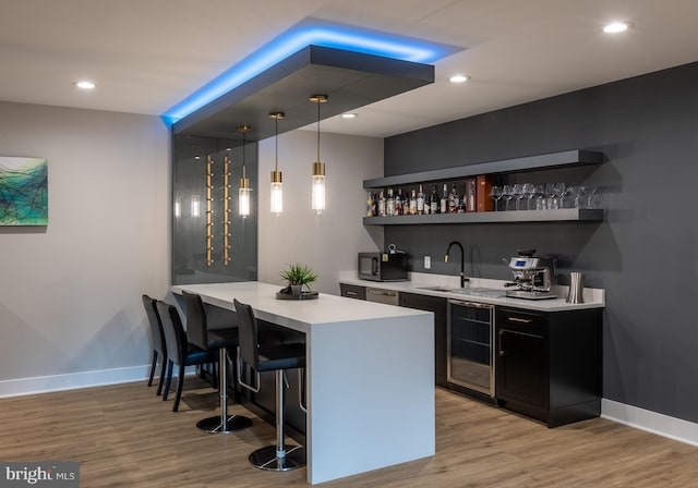 bar with pendant lighting, sink, beverage cooler, stainless steel dishwasher, and light wood-type flooring