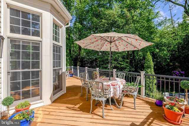 deck with outdoor dining area and view of wooded area