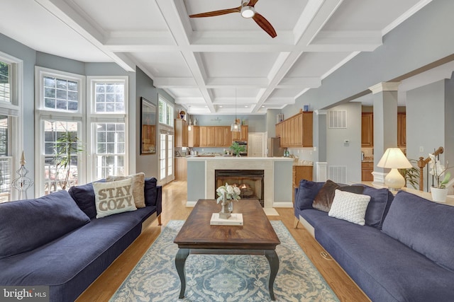 living room with healthy amount of natural light, coffered ceiling, beamed ceiling, ceiling fan, and light wood-style floors