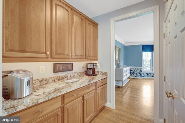 kitchen with light wood finished floors, light stone counters, crown molding, and baseboards