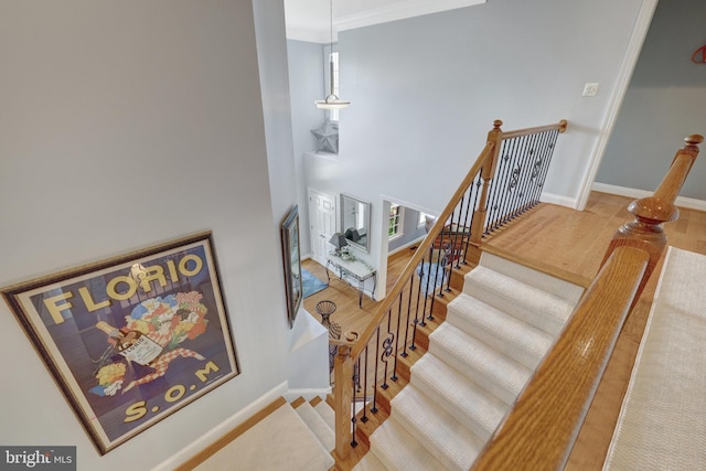 stairway featuring wood finished floors, baseboards, ornamental molding, and a towering ceiling