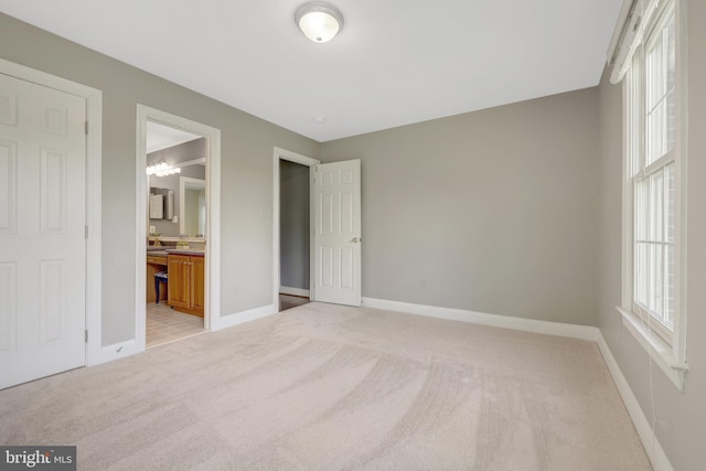 unfurnished bedroom with light carpet, baseboards, and ensuite bathroom