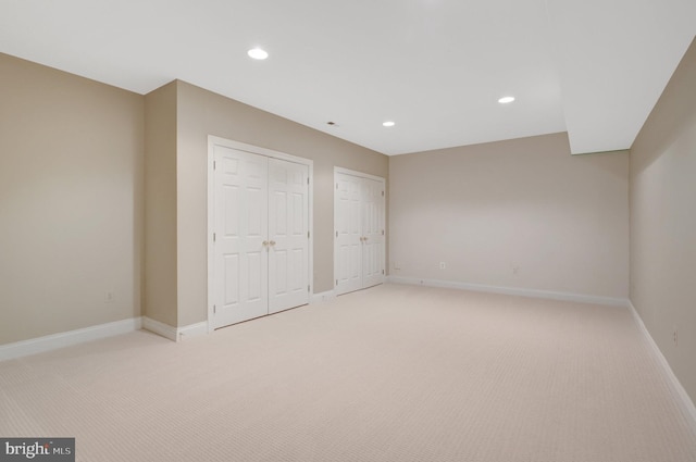 unfurnished bedroom featuring light carpet, two closets, recessed lighting, and baseboards
