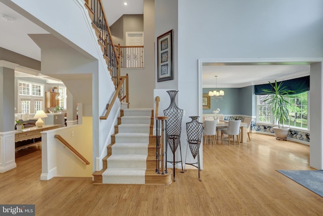 staircase with recessed lighting, baseboards, an inviting chandelier, a towering ceiling, and wood finished floors