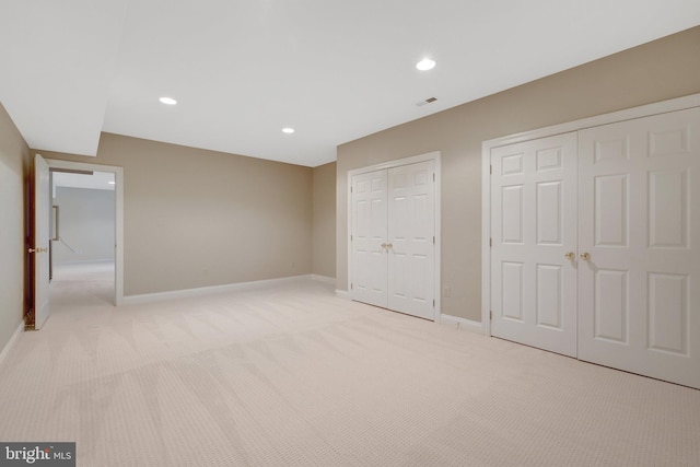 unfurnished bedroom featuring two closets, light carpet, baseboards, and recessed lighting