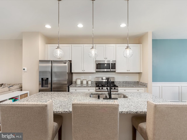 kitchen featuring a breakfast bar, appliances with stainless steel finishes, white cabinets, a center island with sink, and decorative light fixtures