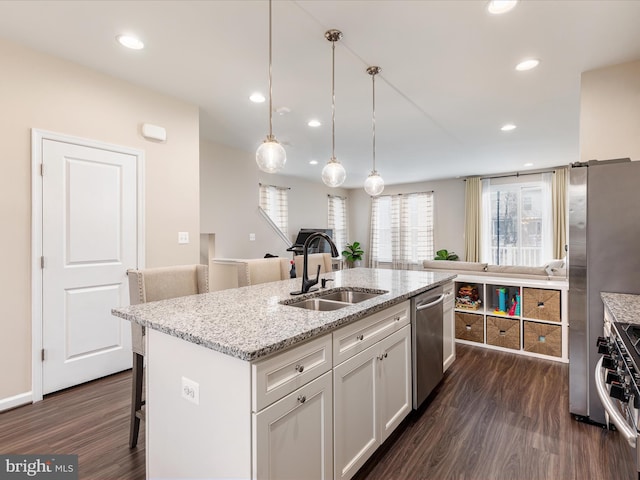 kitchen featuring sink, white cabinets, light stone counters, stainless steel appliances, and a center island with sink