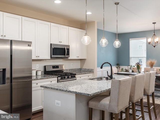 kitchen with a kitchen island with sink, light stone countertops, stainless steel appliances, and white cabinets