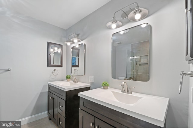 full bath with a stall shower, two vanities, a sink, and baseboards