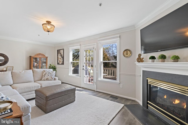 living area featuring wood finished floors, visible vents, baseboards, a glass covered fireplace, and crown molding