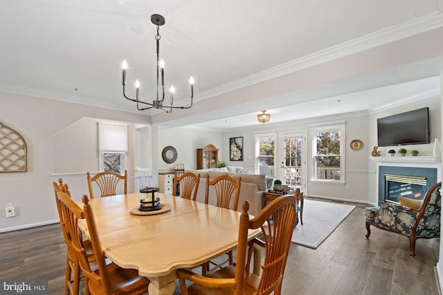 dining space with an inviting chandelier, ornamental molding, a glass covered fireplace, wood finished floors, and baseboards