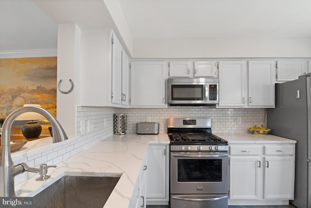 kitchen featuring light stone counters, a sink, white cabinets, appliances with stainless steel finishes, and backsplash