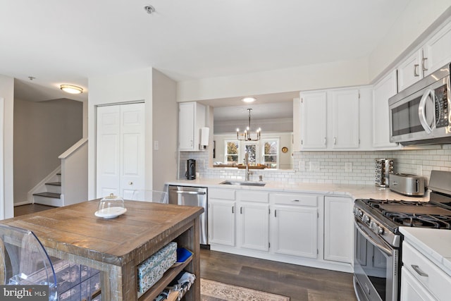 kitchen with appliances with stainless steel finishes, white cabinets, a sink, and a notable chandelier