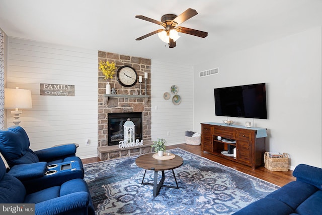 living room featuring wood-type flooring, a stone fireplace, and ceiling fan