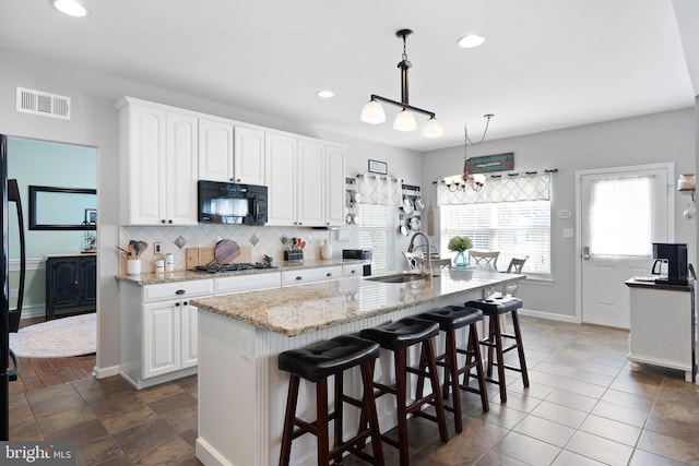 kitchen featuring sink, light stone counters, decorative light fixtures, an island with sink, and white cabinets